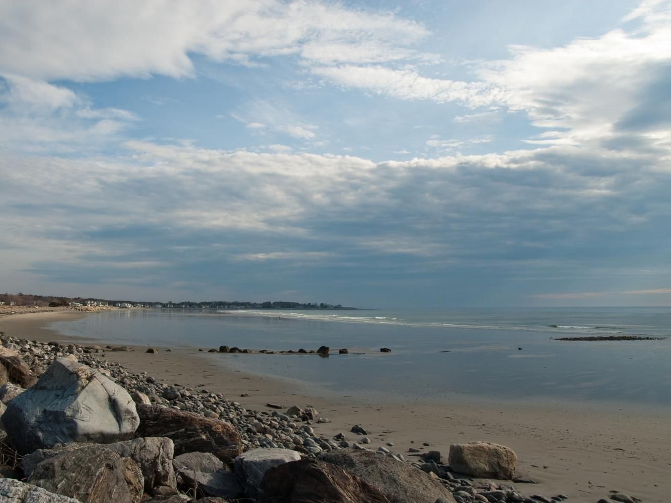 Serene beach scene with scattered rocks, calm water, and a cloudy sky near Meadowmere Resort