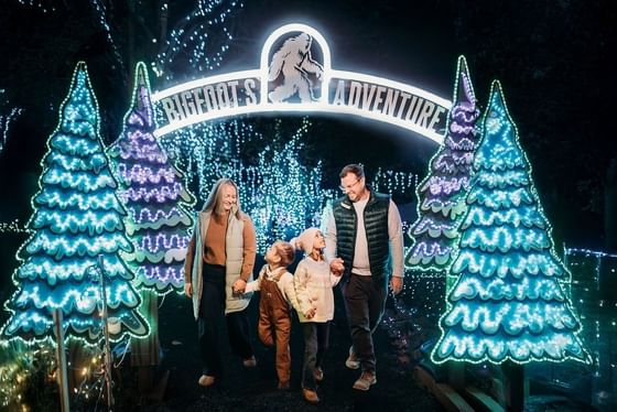 Family of four walking under illuminated Bigfoot Adventure sign at Oregon Garden Resort