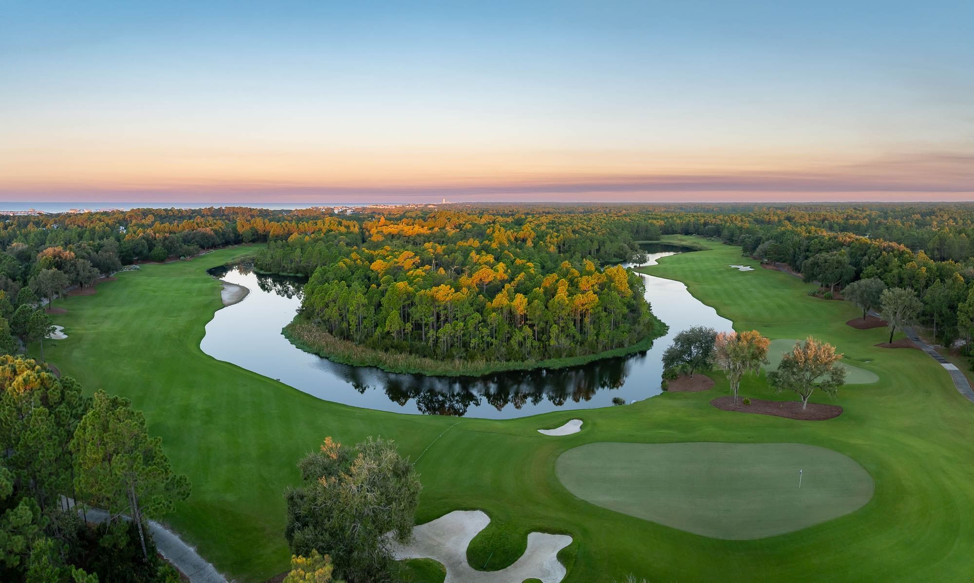 Aerial view of a golf course with lush green fields, ponds, and trees under a twilight sky.