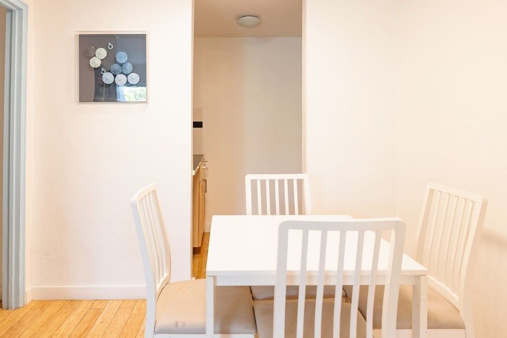 A bright and airy junior suite with a dining table and chairs, artwork on the wall, and a kitchenette in the background.