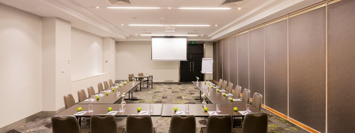 U-shaped table setup facing projector screen in Protea at Novotel Sydney International Airport