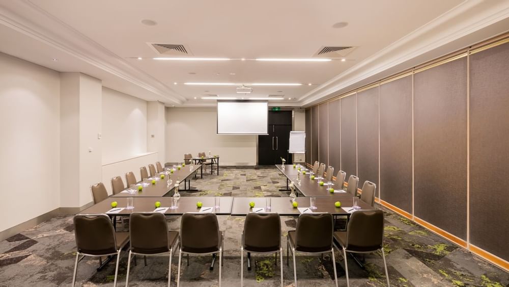 U-shaped table setup facing projector screen in Protea at Novotel Sydney International Airport
