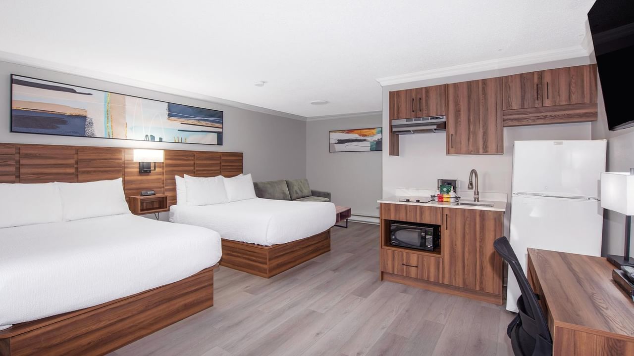 Hotel guest room with two queen beds, a sofa, kitchenette, work desk and flat-screen TV.
