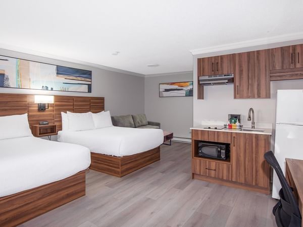 Hotel guest room with two queen beds, a kitchenette with a refrigerator and microwave, a sofa and a work desk.
