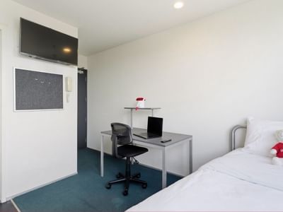 A tidy room with a bed, desk, laptop, and bear mascot at Student Living Auckland – Anzac.