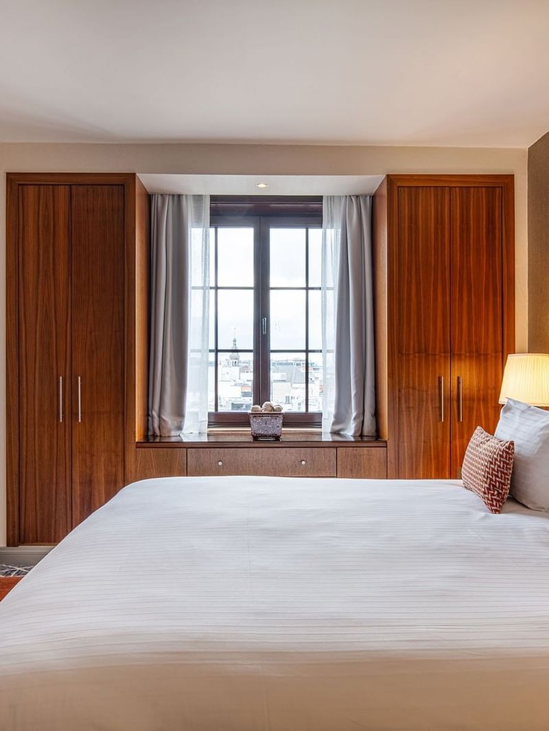 Warwick Suite featuring a bed placed by tall windows under a warm lamp light at Warwick Grand Place Brussels