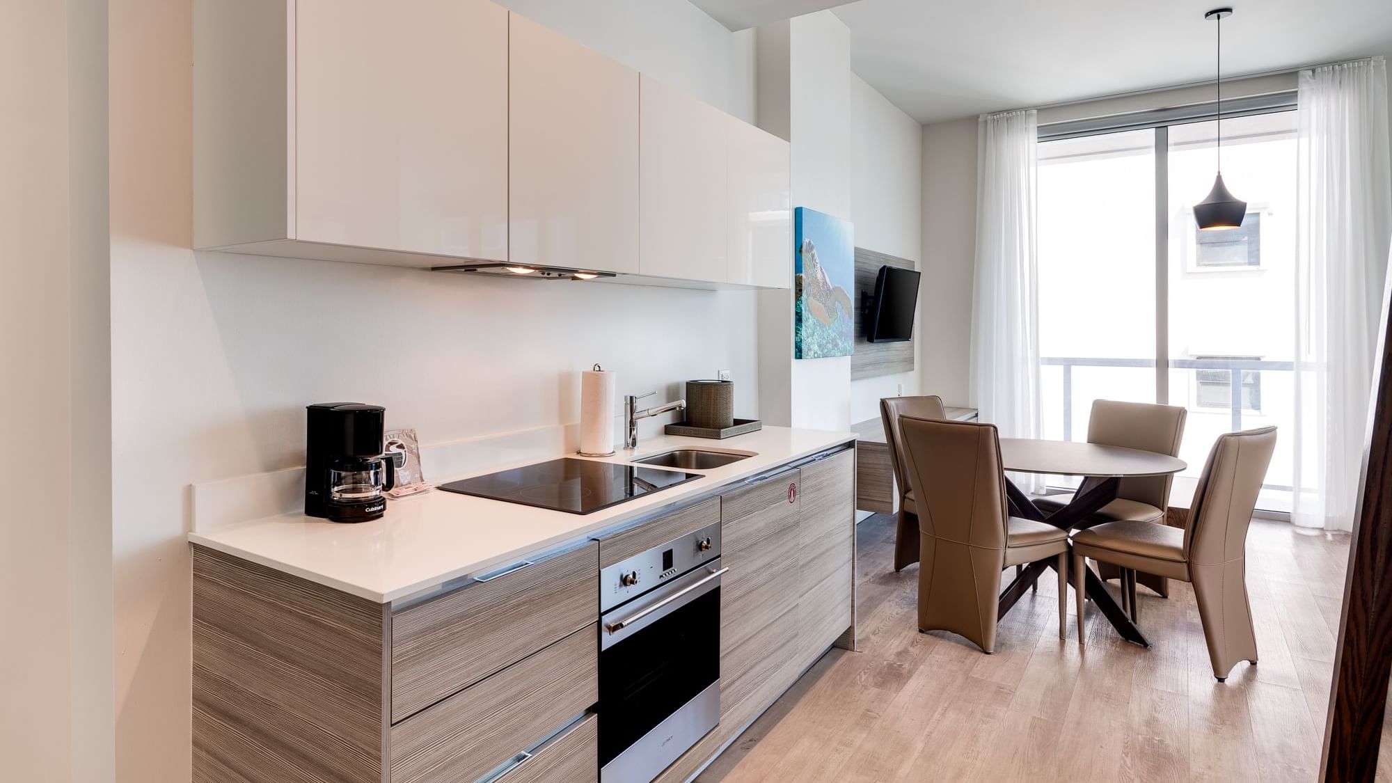A modern kitchen with a dining area, featuring a coffee maker, sink, stove, oven, and a dining table with four chairs.