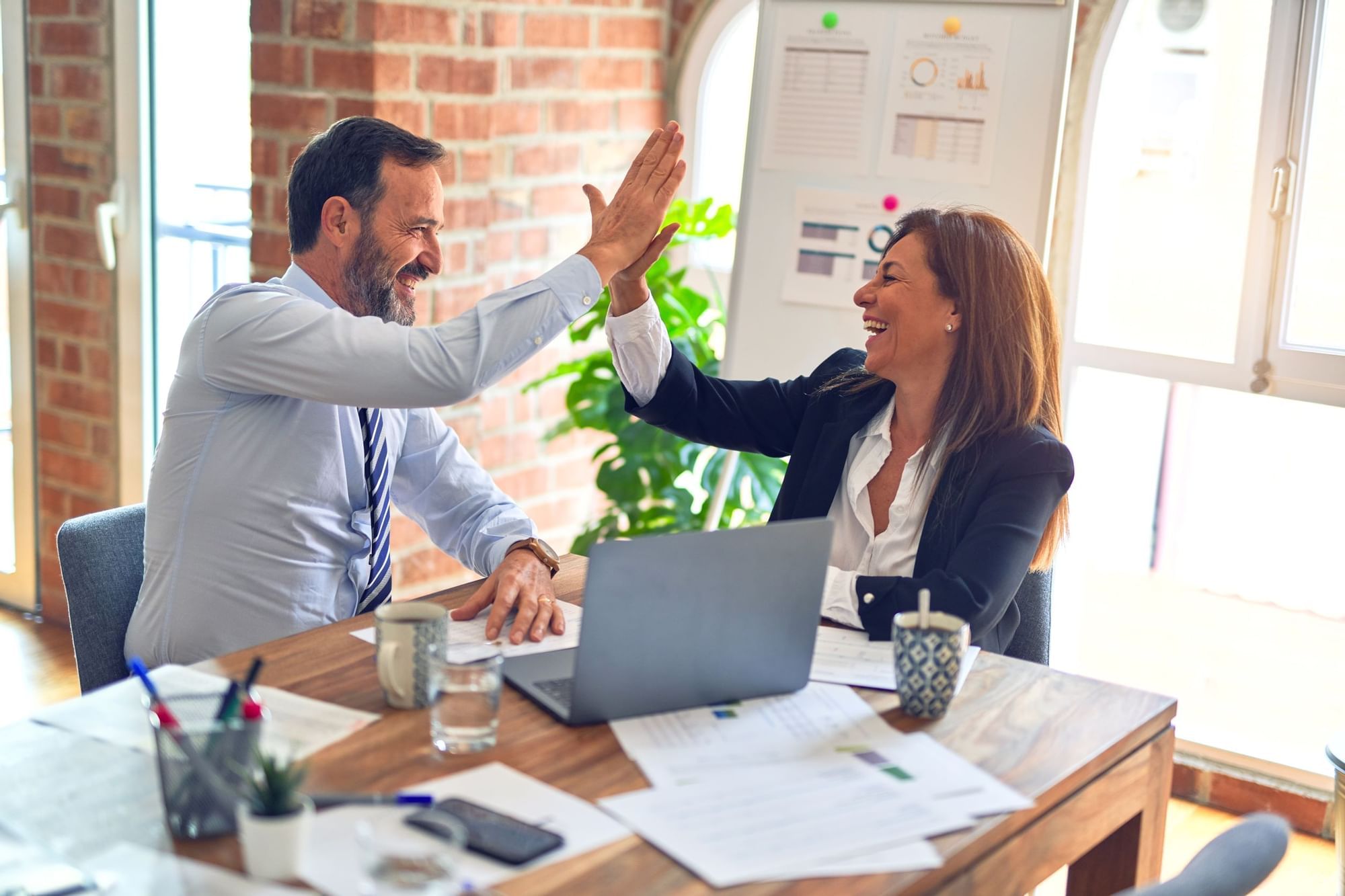 Business duo high-fiving in a conference table with laptop and documents at the Novotel Sunshine Coast Resort