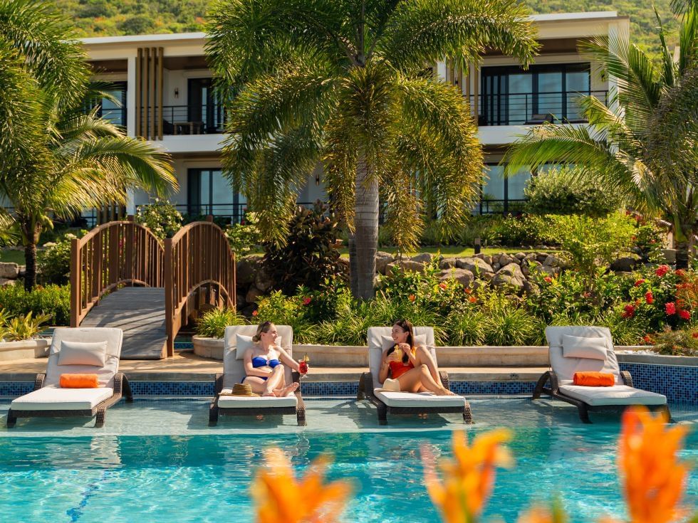 Two women relax on lounge chairs by a pool, surrounded by palm trees and flowers at Golden Rock Resort