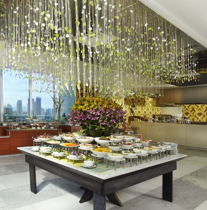 Mesa buffet de Bazaar con cuencos blancos bajo una lámpara de cuentas, junto al florero cerca de Megapolis Hotel Panama