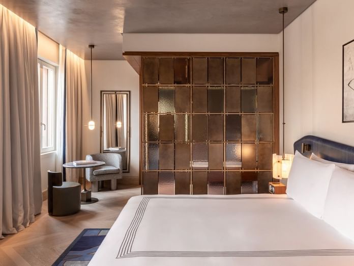 Deluxe king bed room with bronze glass partition, seating area, and modern decor at The Thompson Rome, Roma
