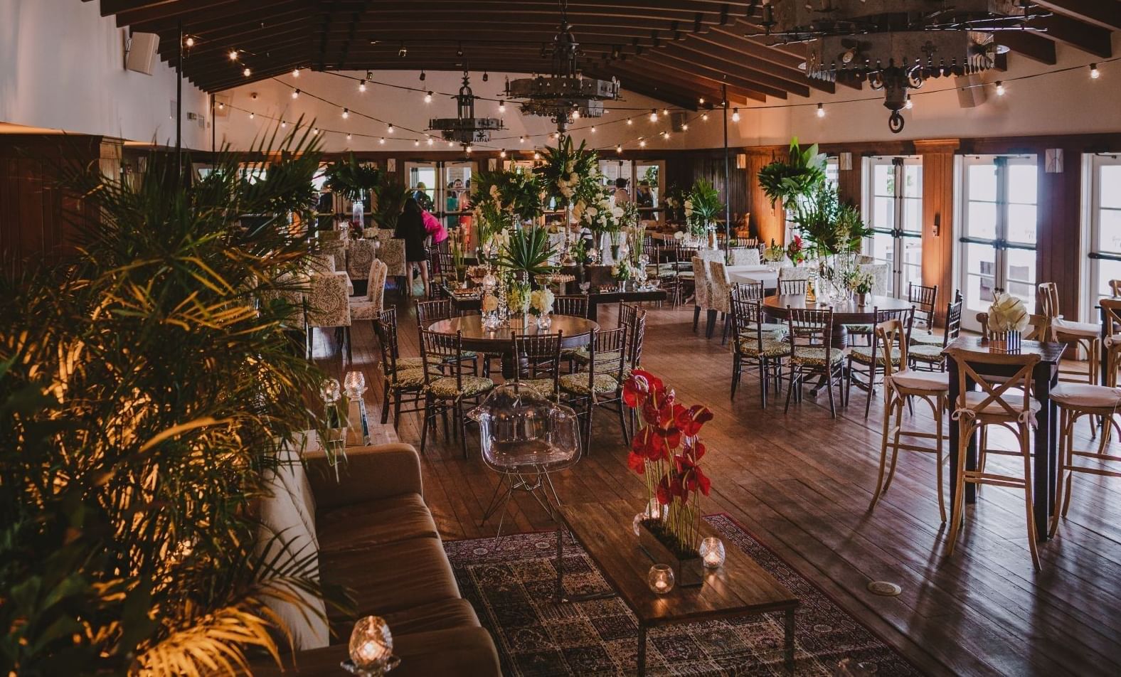 a large dining room with round tables and chairs, floral arrangements, and string lights