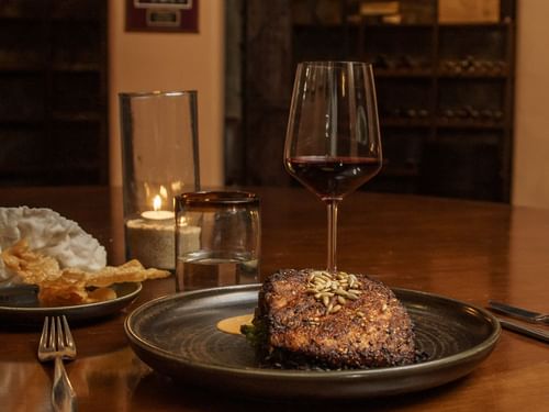 Dinner setting with a seared steak, glass of red wine, and a candle at La Cava de Santiago in Hacienda del Mar Los Cabos.