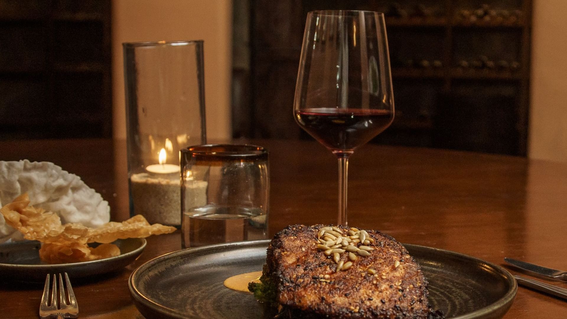 Dinner setting with a seared steak, glass of red wine, and a candle at La Cava de Santiago in Hacienda del Mar Los Cabos.