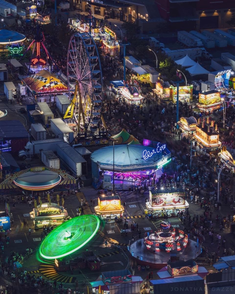 Aerial view of illuminated carnival at night with glowing ferris wheel and colorful amusement rides near Hotel X Toronto