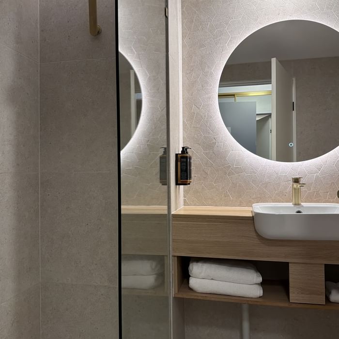 Modern bathroom with shower, vanity, and round mirror at Mercure Charlestown.