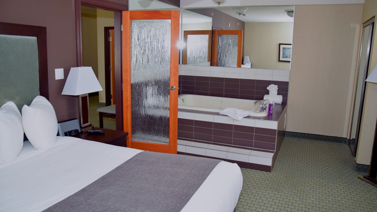 Hotel room with bed, lamp, jetted tub, and glass door.