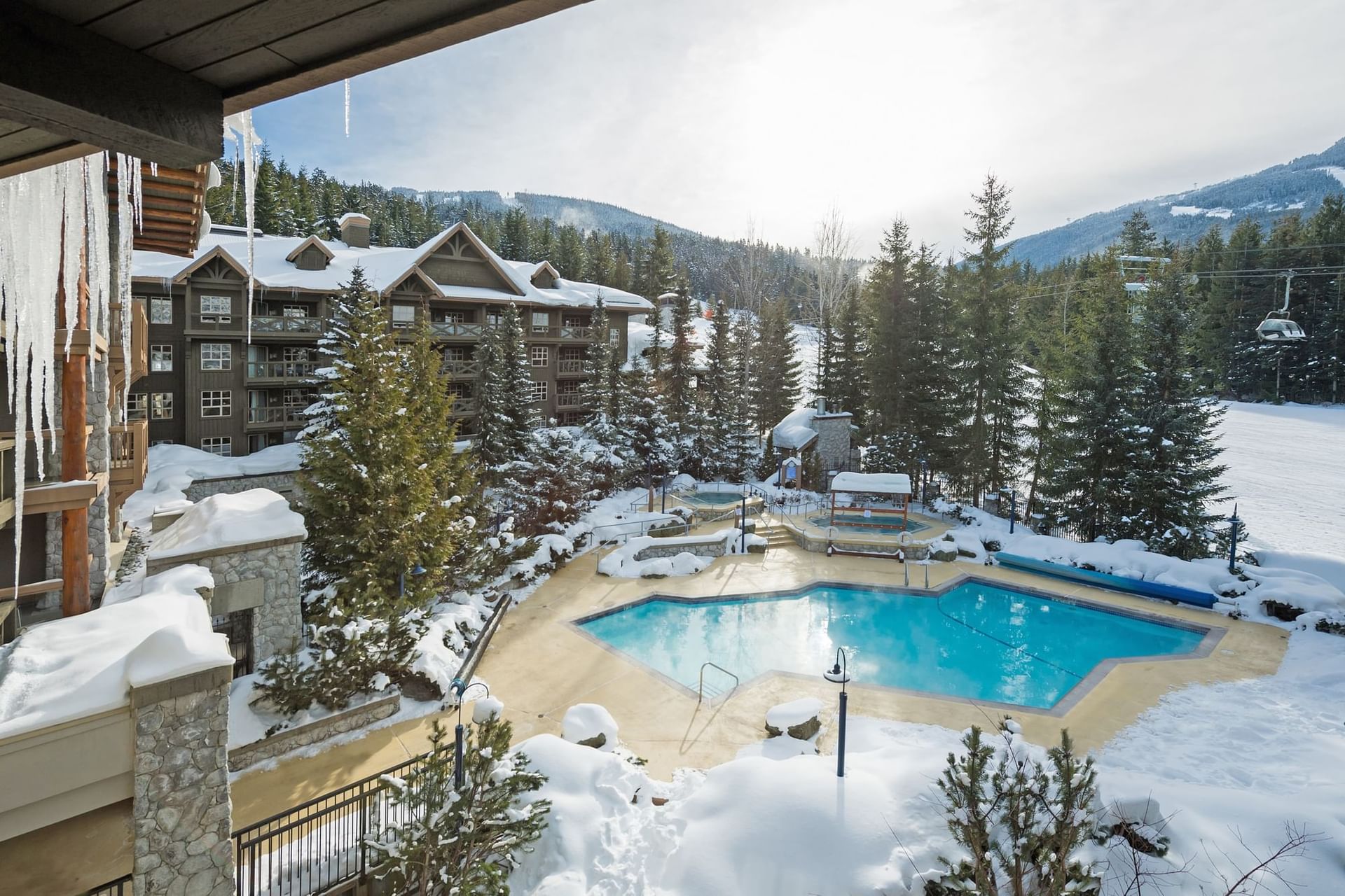 Blackcomb Springs Suites with a snow-covered pool area surrounded by trees, a mountain backdrop