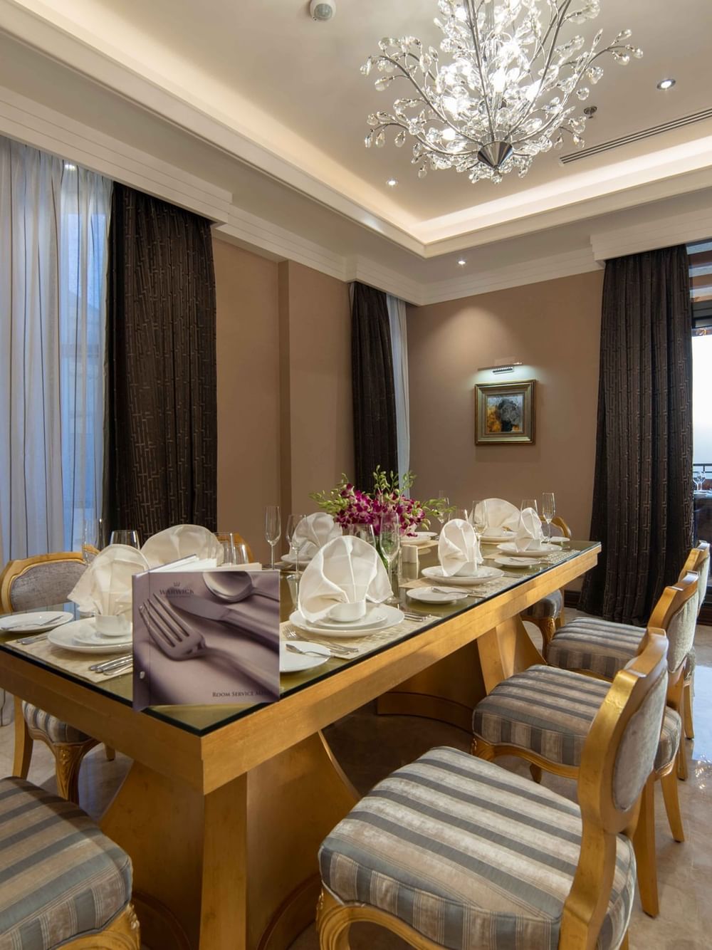 Gilded dining set by floor-to-ceiling curtains under a sprawling crystal chandelier in Penthouse Villa at Warwick Al Khobar