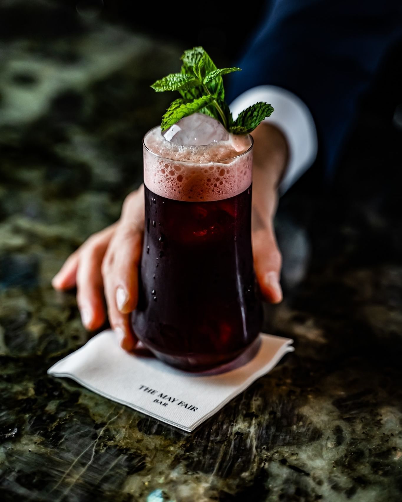 Bar man holding a cocktail of the Arabia Souk with mint garnish at The May Fair Bar.