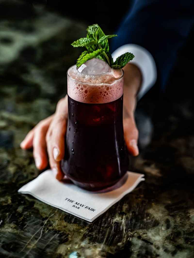 Bar man holding a cocktail of the Arabia Souk with mint garnish at The May Fair Bar.