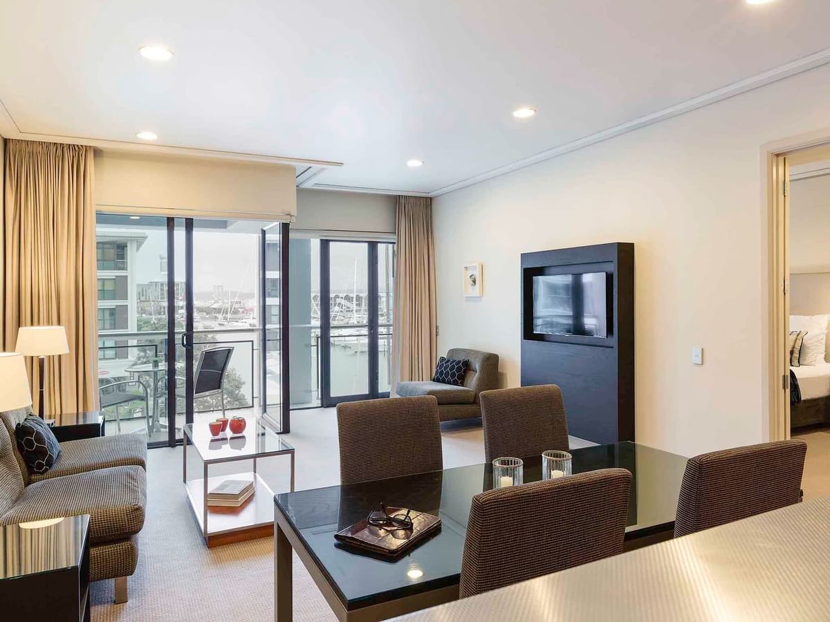 TV lounge and a dining table by the window in the Executive Deluxe One Bedroom Suite at The Sebel Auckland Viaduct Harbour