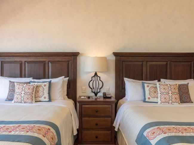 Two cozy beds with wooden headboards, white linens and patterned pillows in One Bedroom Villa at Hacienda Del Mar Los Cabos.