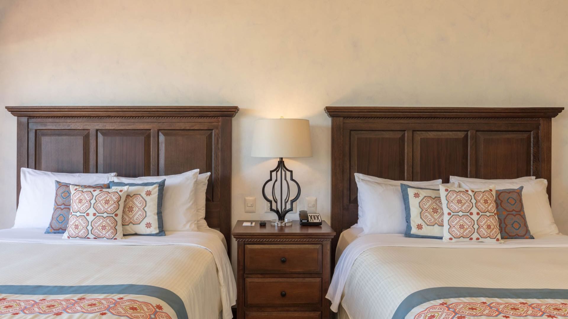 Two cozy beds with wooden headboards, white linens and patterned pillows in One Bedroom Villa at Hacienda Del Mar Los Cabos.