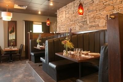 Leather booths facing a stone wall with tables illuminated by warm red pendant lights at Hilltop Inn Salmon Arm