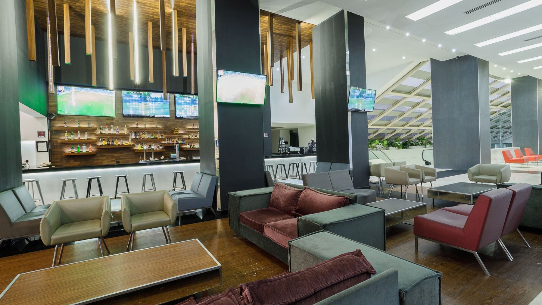 Sofas by a wooden table under hanging wood slats and a hanging TV in the Stock Bar at Real Inn Tijuana