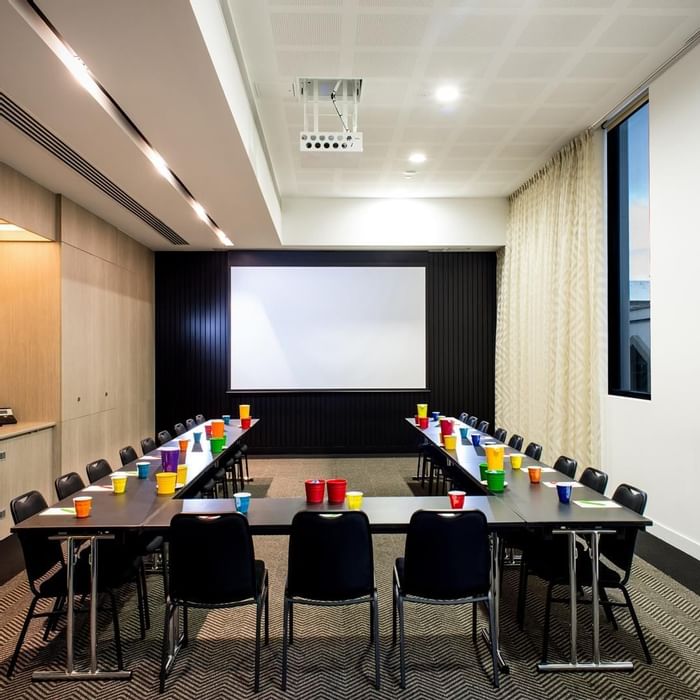 U-shape table set-up facing a large screen in The Engine Room at Ibis Adelaide