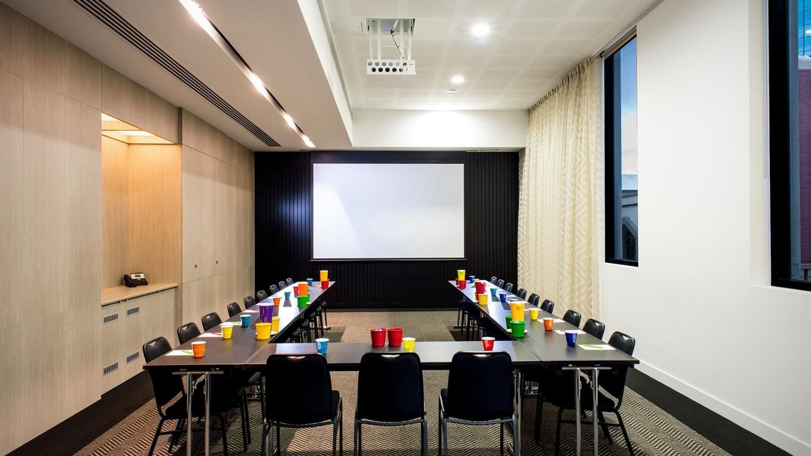 U-shape table set-up facing a large screen in The Engine Room at Ibis Adelaide