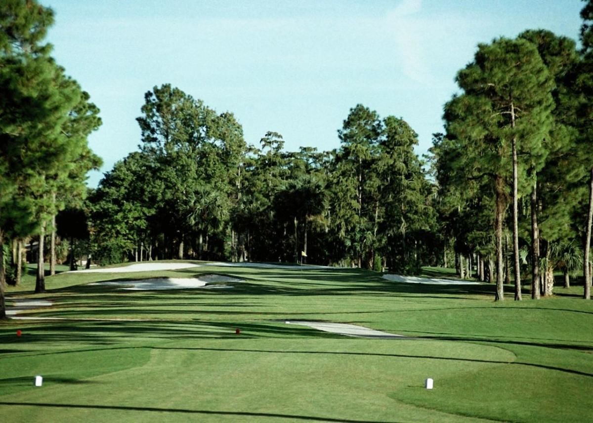 A wide view of a golf course with trees and sand traps.