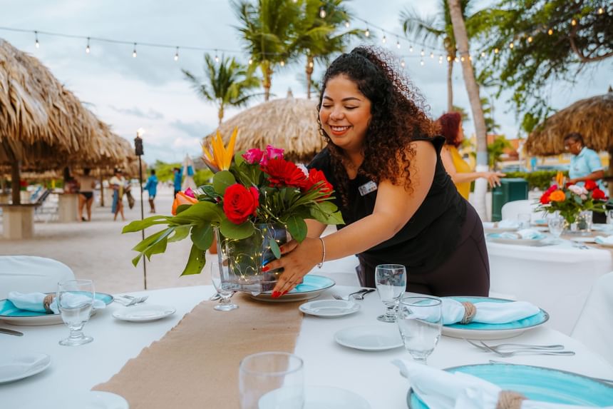 Lady placing a flower vase on a table set outdoors overlooking the beach at Passions on the Beach