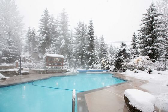 Pool outdoors surrounded by snowy trees at Blackcomb Springs Suites