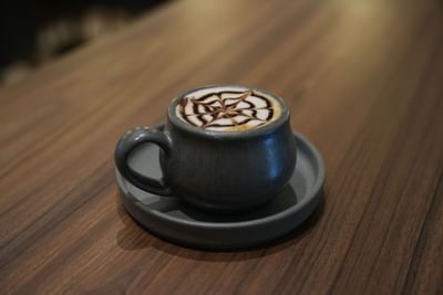 Ceramic cup filled with latte art resembling a star pattern, on a wooden table at in Cafe Farallones at Dann Carlton Cali