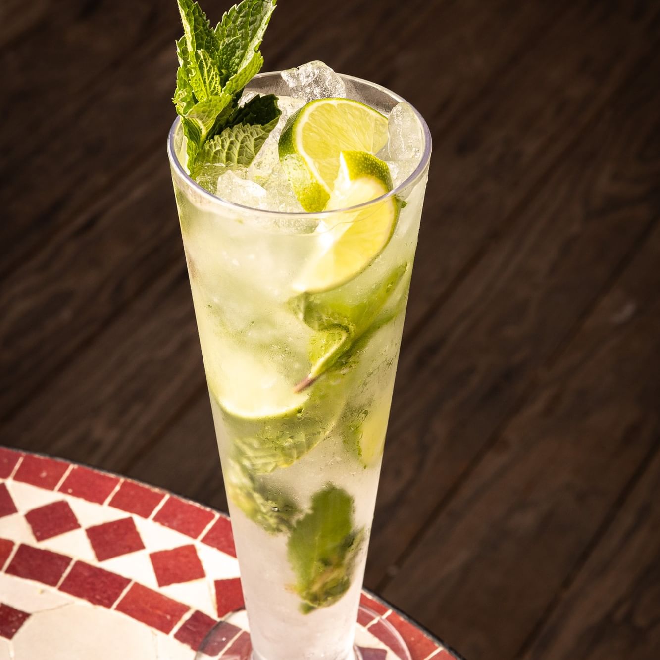 A refreshing mojito cocktail with fresh mint, lime slices, and ice in a tall glass on a mosaic tile table.
