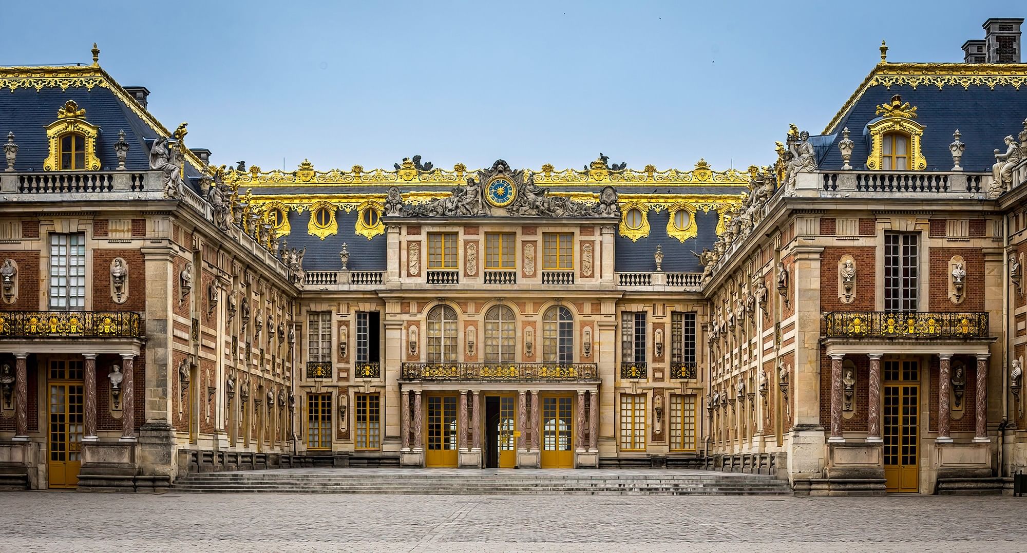 Palace of Versailles exterior featuring gold ornate details above stone walls near Hotel Westminster Paris