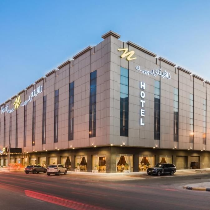 L'immeuble « Modern Naviti » de Warwick Al Khobar, avec son enseigne lumineuse et des voitures garées devant, au crépuscule