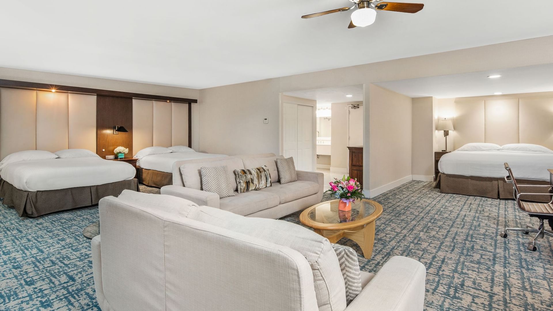 A wide view of a hotel suite with two beds, a sofa, and a coffee table.