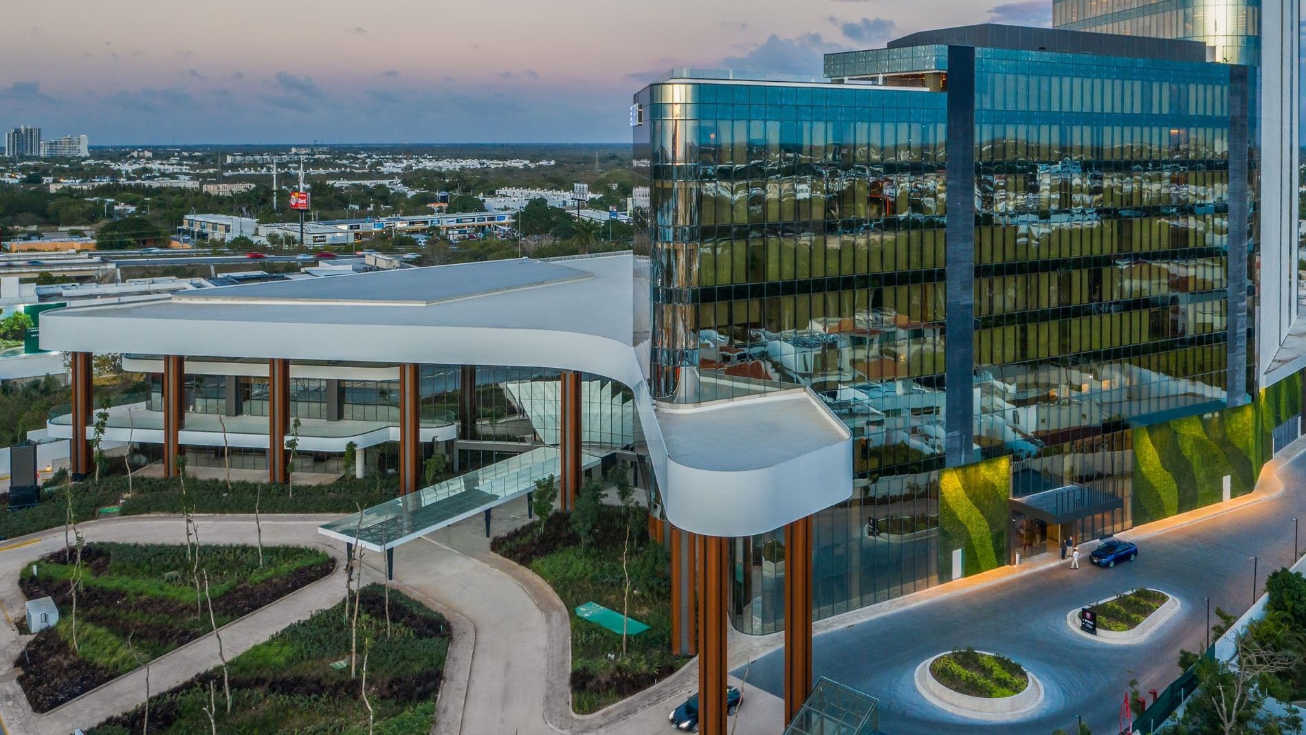 Exterior view of the entrance at twilight, highlighting the sleek, glass architecture at Camino Real Merida