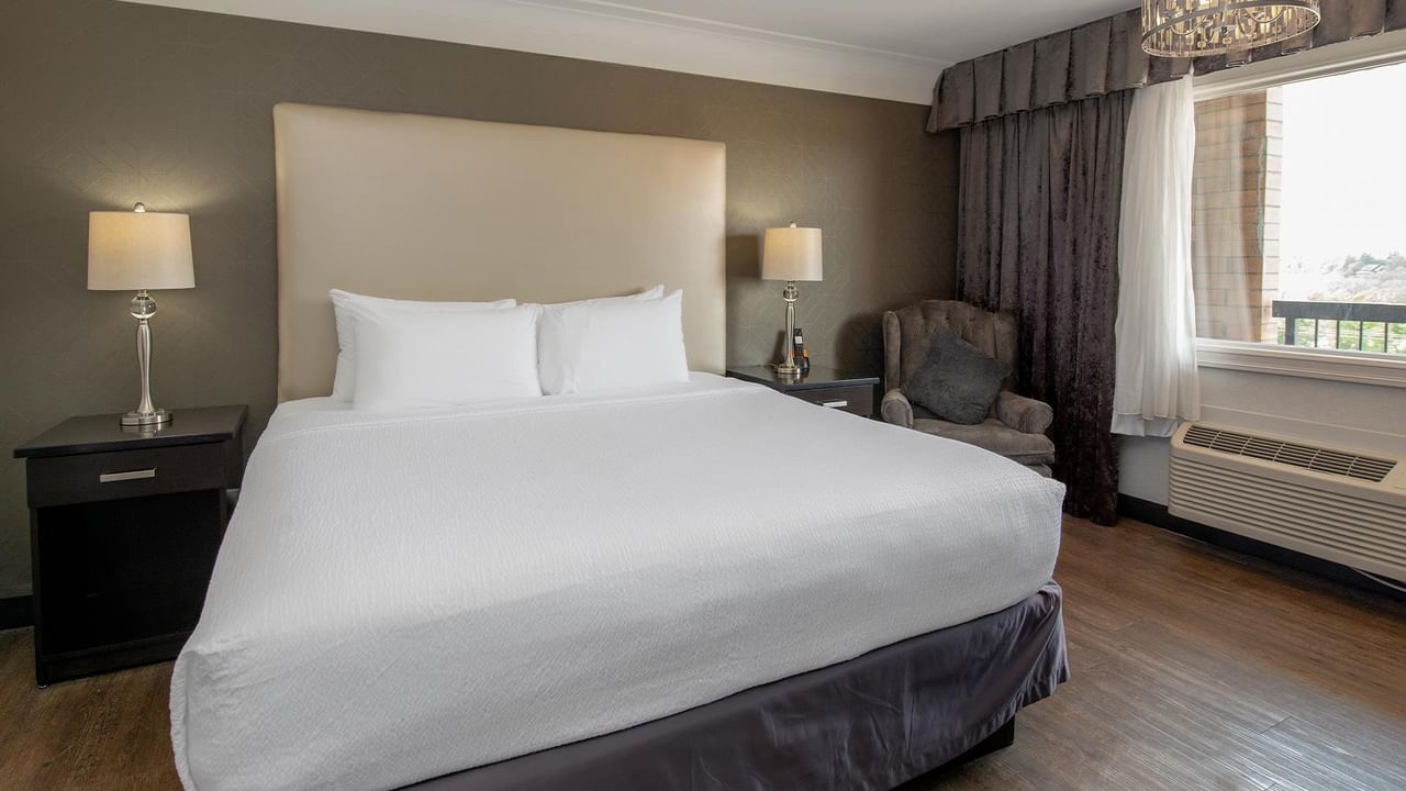 Modern guest room with king bed, gray upholstered headboard, and elegant lighting at Coast Calgary University Area Hotel by APA