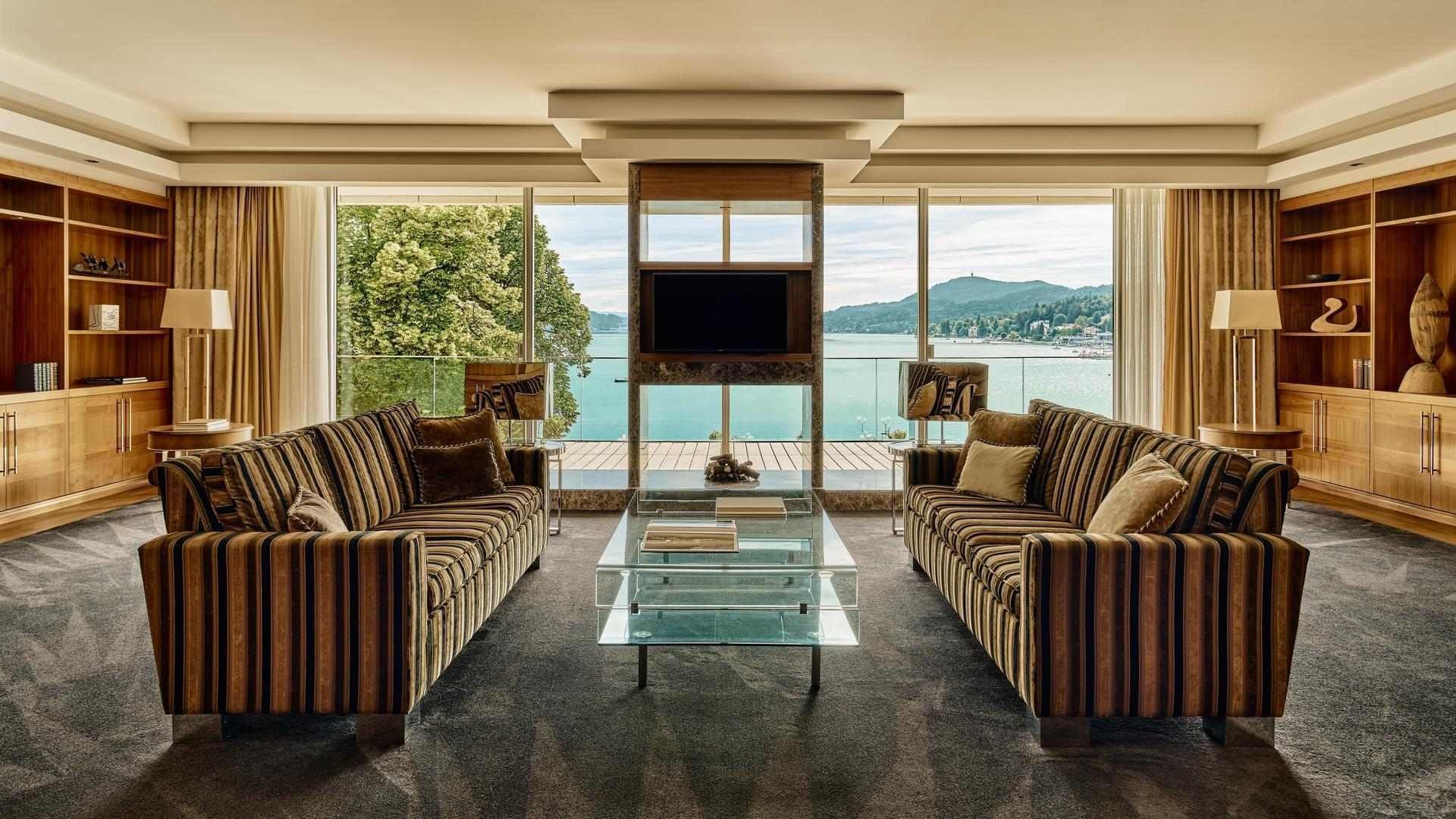 Wohnzimmer mit zwei Sofas, Glastisch und Panoramablick auf den See und die Berge.
