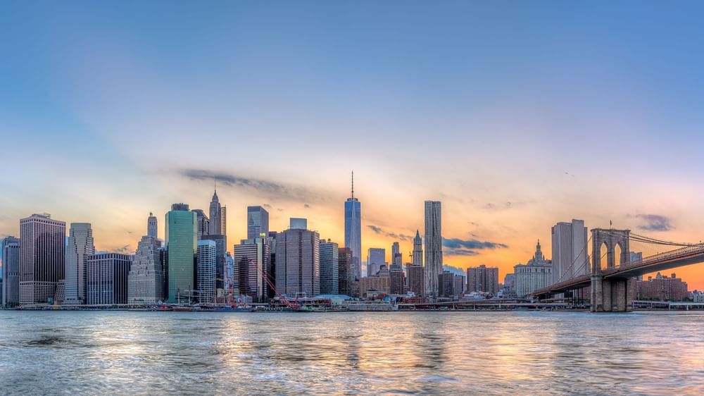 New York City skyline at sunset with a bridge over the East River.