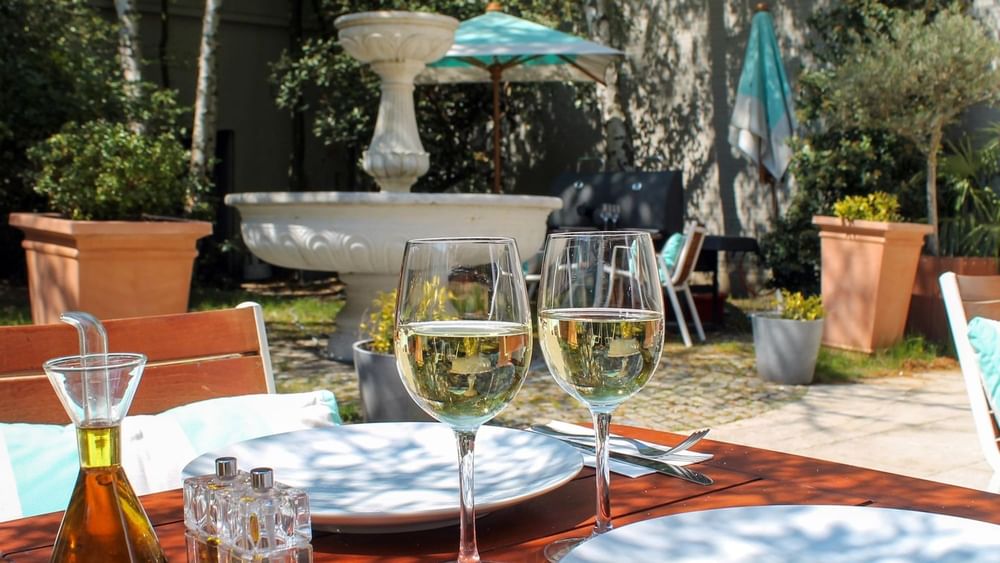 White wine glasses on a sunlit terrace table by the fountain at Hotel Barsey by Warwick