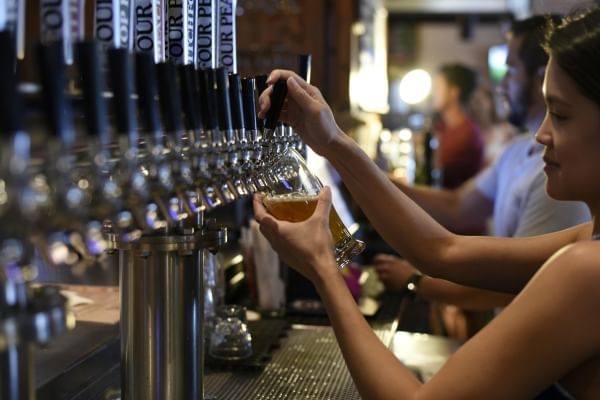 A woman pulls a beer from a tap wall in a bar. 