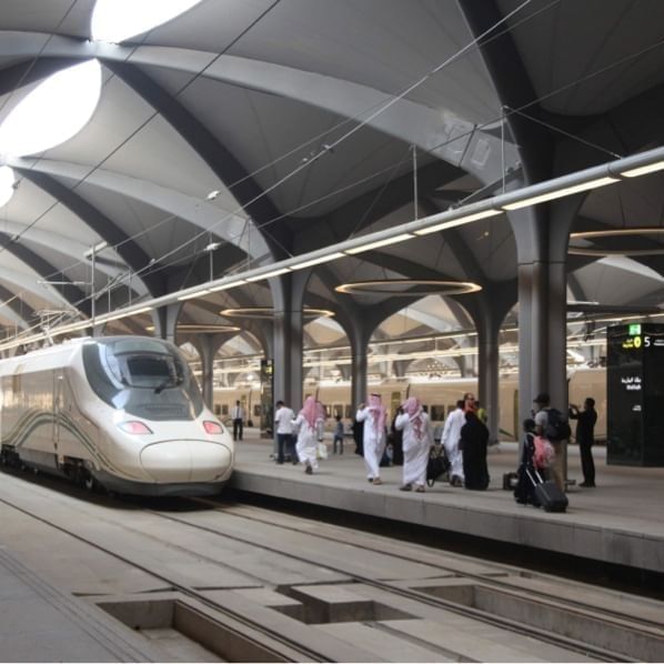Haramain Railway Station with arched ceilings, a sleek train, and people walking with luggage near Warwick Hotel Jeddah