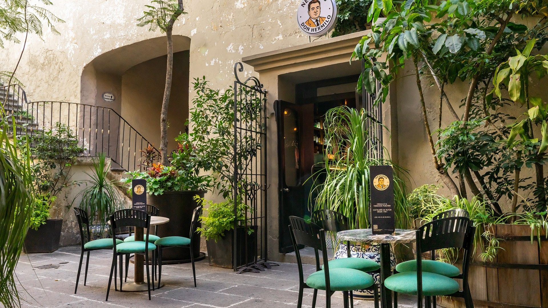 Charming outdoor cafe patio with green cushioned chairs, potted plants, and stone walls at Quinta Real Puebla