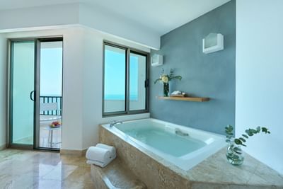 An elegant indoor whirlpool tub next to glass doors opening to a scenic resort balcony view.