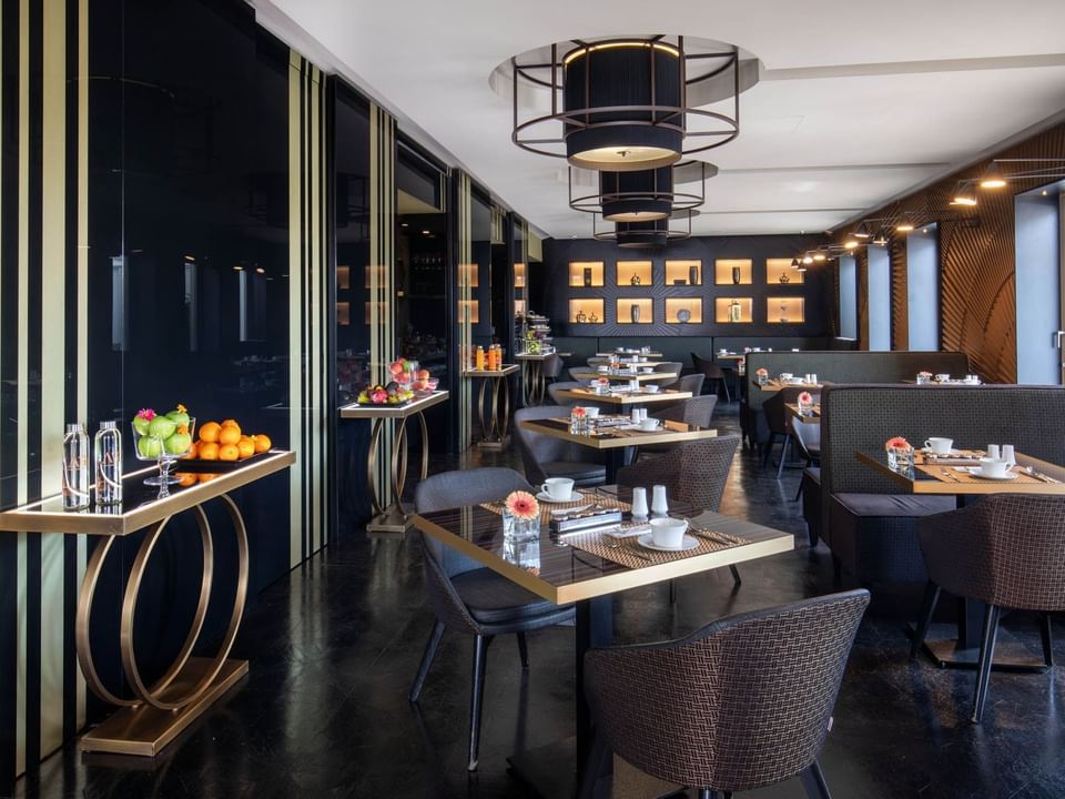 Modern dining area with stylish furniture, fruit displays, and ambient lighting at The Glam Hotel